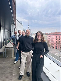 Five people posing in a group photo on the balcony of an office building