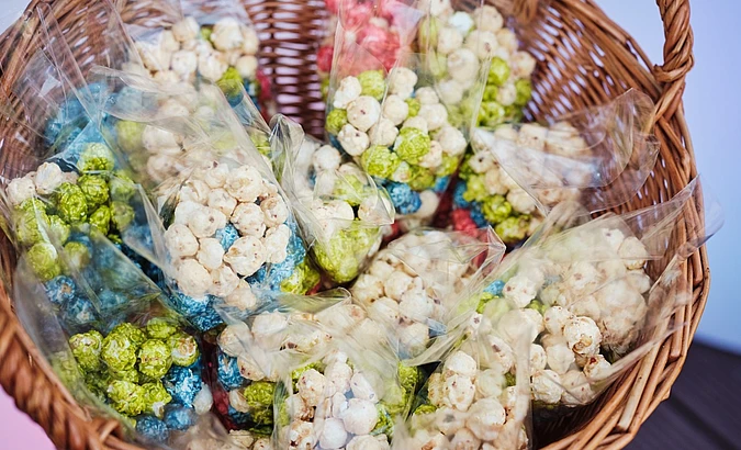 Wicker basket filled with cellophane bags of popcorn in various colors including white, green, blue, and pink