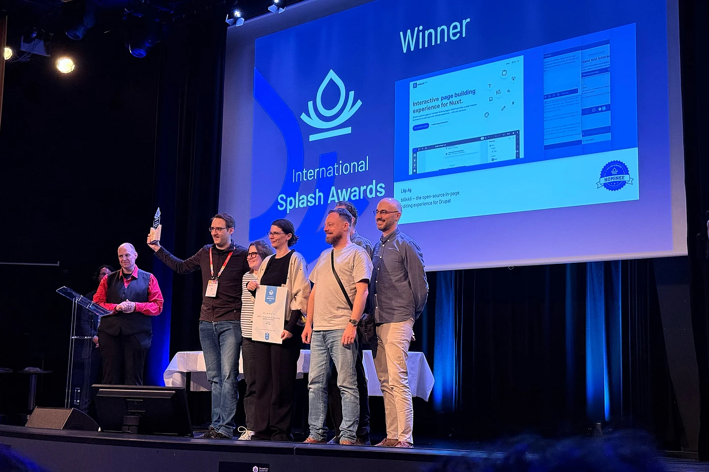 Team receiving International Splash Awards winner certificate on stage with blue backdrop and presentation screens