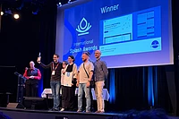 Team receiving International Splash Awards winner certificate on stage with blue backdrop and presentation screens