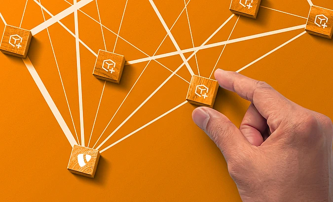Wooden blocks with extension icons on orange background. One with the TYPO3 logo. A hand hold one block. White lines connect the blocks.