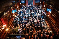 Large group of business professionals waving at camera during awards ceremony in ornate hall