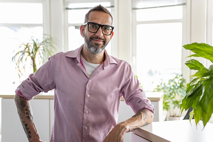 A half-portrait image of André Richter, standing next to a plant in an office