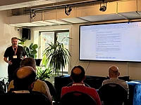 Man presenting to audience in modern office with large screen display and plants