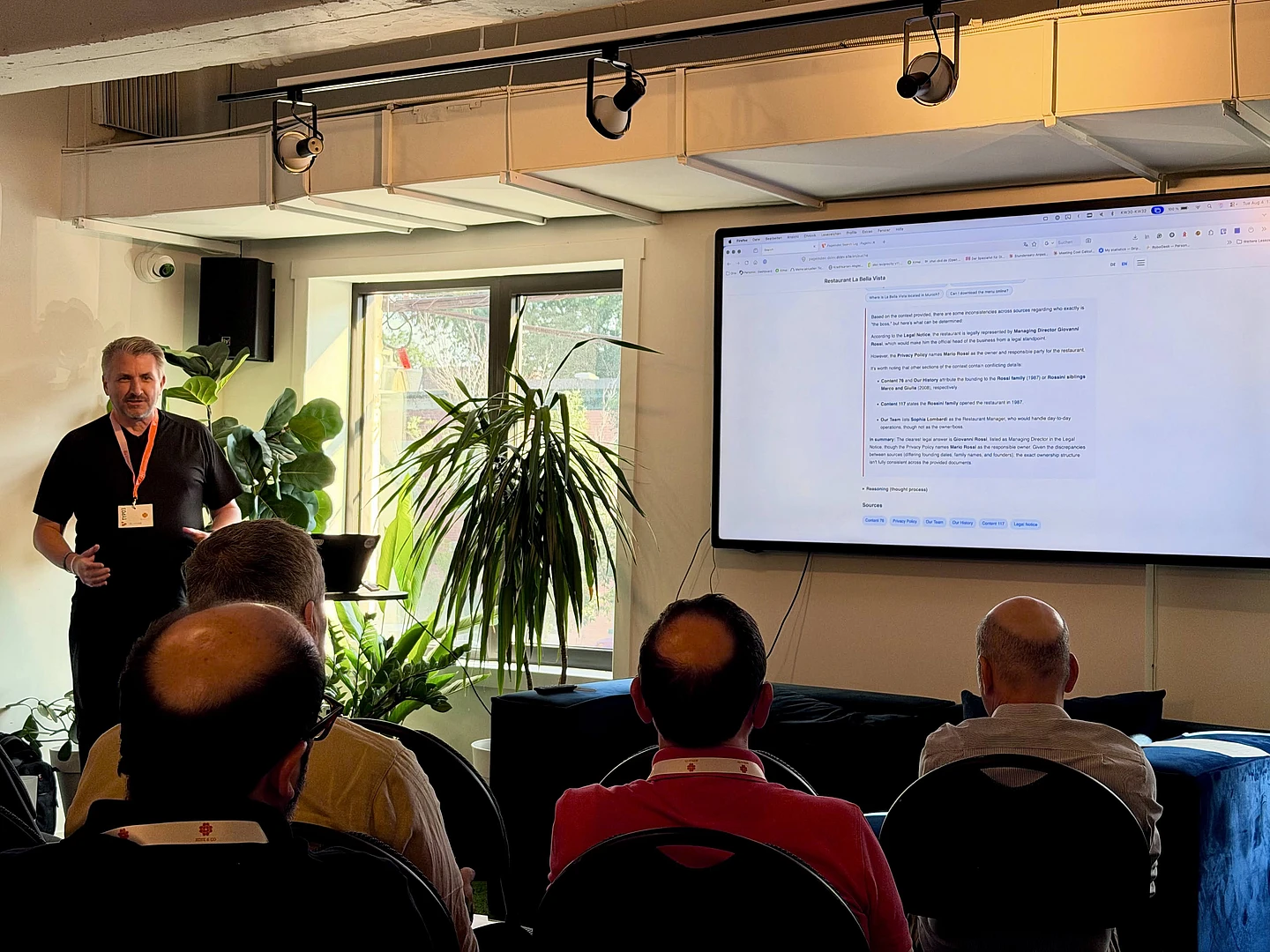 Man presenting to audience in modern office with large screen display and plants