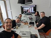 Group of people at a conference table and more individuals on the screen in the background