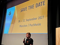 TYPO3camp save the date announcement for September 10-12, 2027 in Munich/Puchheim with speaker presenting on stage