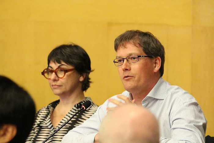 Two people wearing glasses speaking at a panel discussion against a yellow background