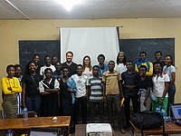 Group photo of diverse students and instructors in a classroom with blackboards and educational materials