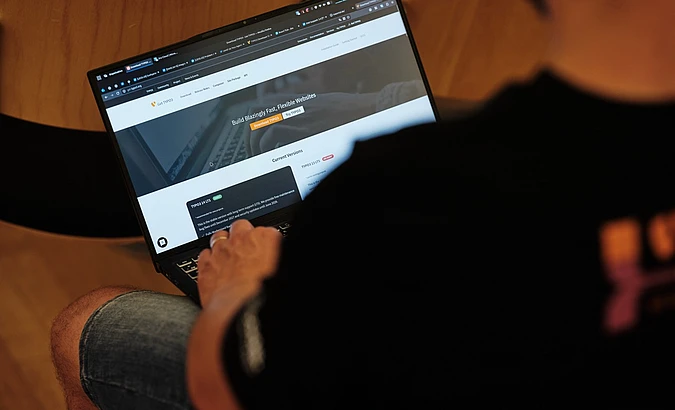 Person hält Laptop mit Website-Builder-Oberfläche und Text 'Build Blazingly Fast, Flexible Websites'