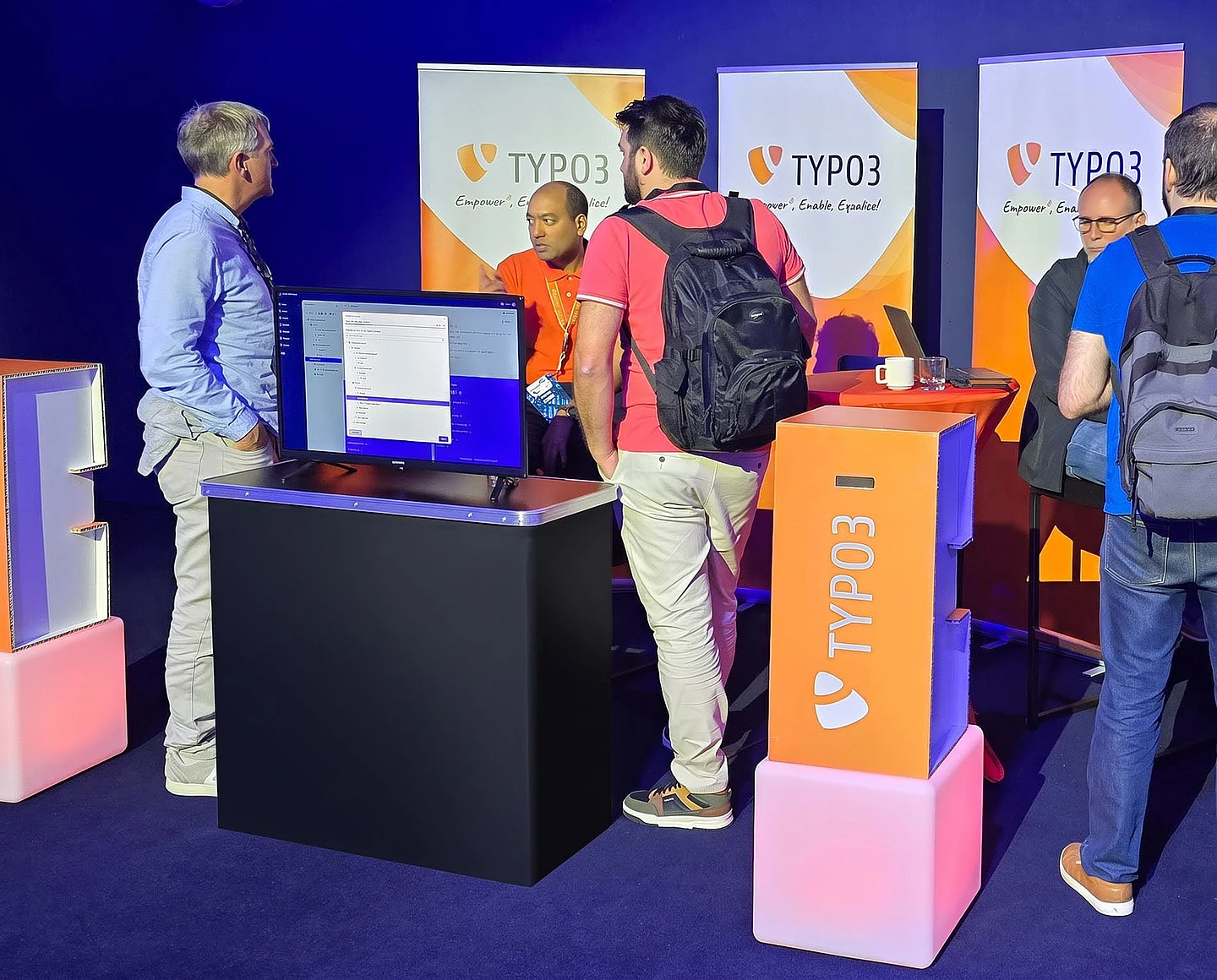 TYPO3 conference booth with visitors interacting at demo station displaying software on monitor