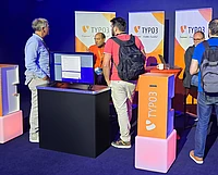 TYPO3 conference booth with visitors interacting at demo station displaying software on monitor