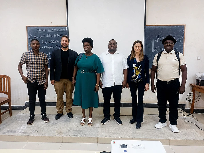 Six people standing in a line in a classroom with chalkboards behind them
