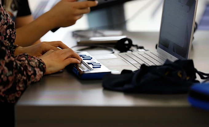 Hands operating a braille display connected to a laptop.
