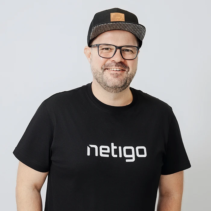 Image of a caucasian male person with glasses, a cap, and a black t-shirt reading "netigo".
