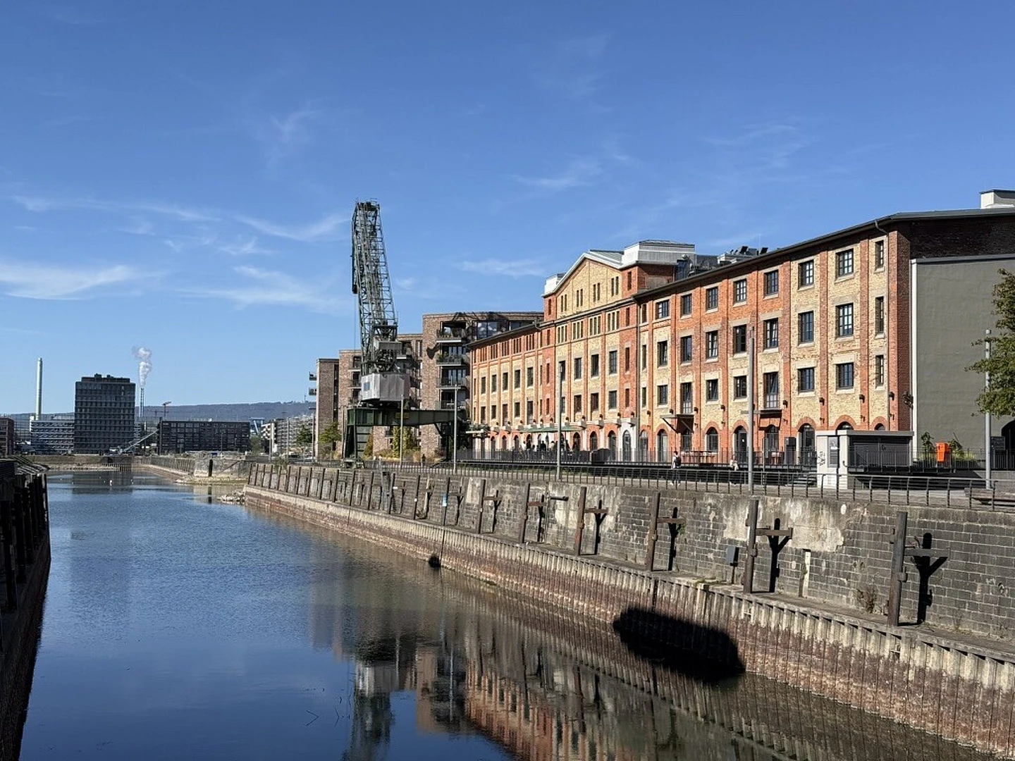 Historic brick warehouse buildings along a canal with vintage industrial crane and stone waterfront wall under blue sky