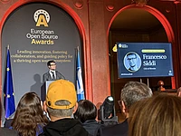 Speaker at European Open Source Awards ceremony with audience watching presentation on stage with red arch backdrop