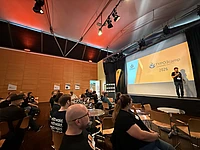 Speaker presenting at TYPO3camp Munich 2026 conference in modern auditorium with audience seated at tables