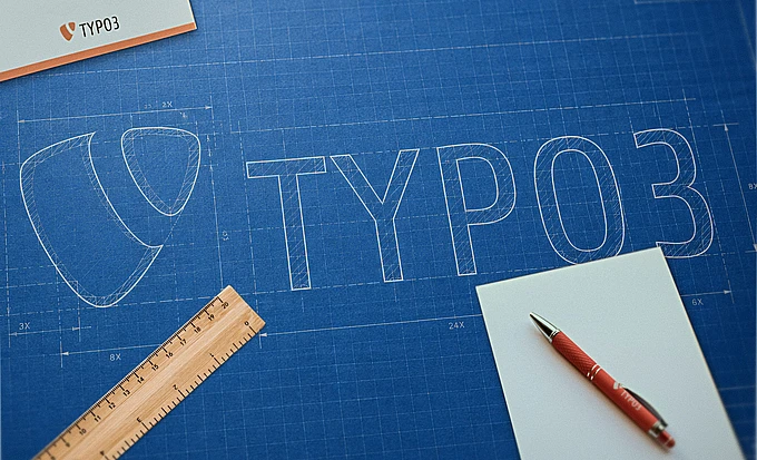 A blueprint features the TYPO3 logo and text sketched in white. A ruler, red pen, and blank white papers are placed on the blueprint, along with a TYPO3-branded card.