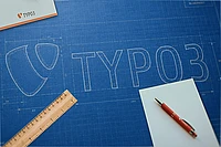 A blueprint features the TYPO3 logo and text sketched in white. A ruler, red pen, and blank white papers are placed on the blueprint, along with a TYPO3-branded card.