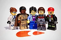 Five LEGO minifigures stand in a row, each with unique outfits and facial expressions, on a white background with an orange TYPO3 logo shape on the floor in front of them.