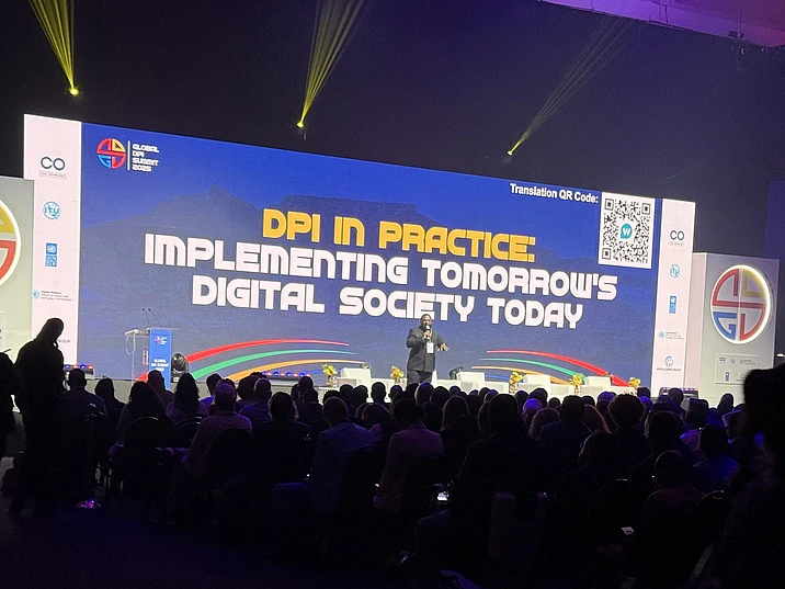 Conference speaker presenting on stage at Global Summit about DPI implementation for digital society, with large audience and blue projection screen