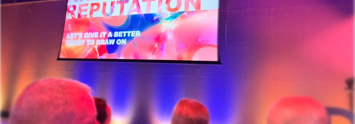 Conference screen displaying text about amplifying outdated reputation with audience silhouettes in colorful lighting
