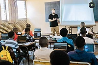 Instructor teaching students in classroom with laptops and projector screen