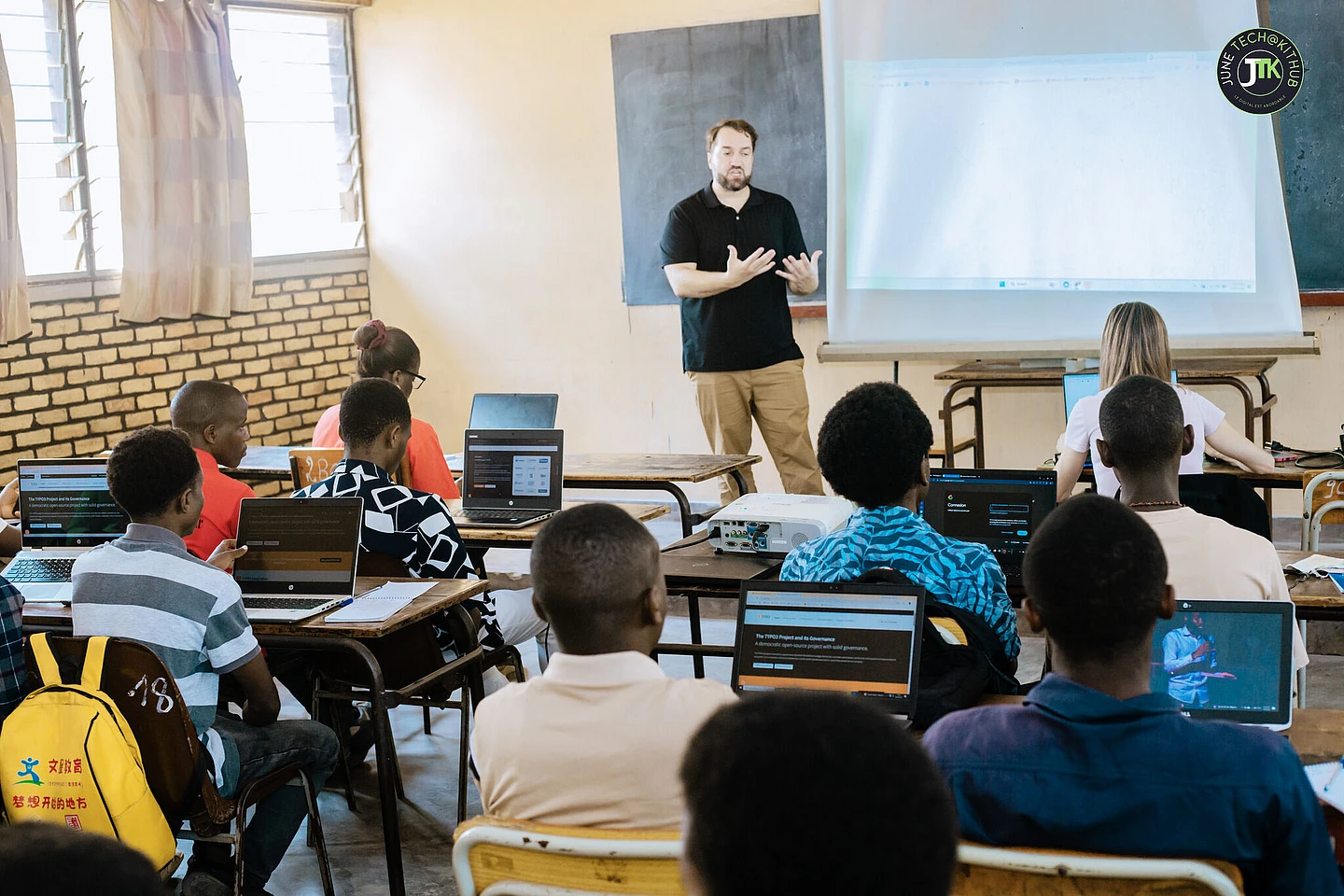 Instructor teaching students in classroom with laptops and projector screen