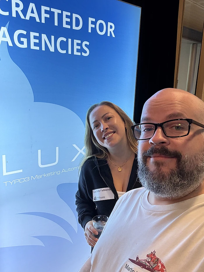Two people at a conference in front of a blue screen displaying 'Crafted for Agencies' and TYPO3 Marketing Automation branding