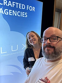 Two people at a conference in front of a blue screen displaying 'Crafted for Agencies' and TYPO3 Marketing Automation branding