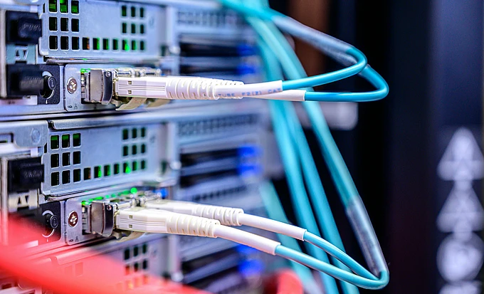 Close-up of network cables connected to server hardware in a data center, with blue, white, and red cables plugged into high-performance server units featuring green status lights.
