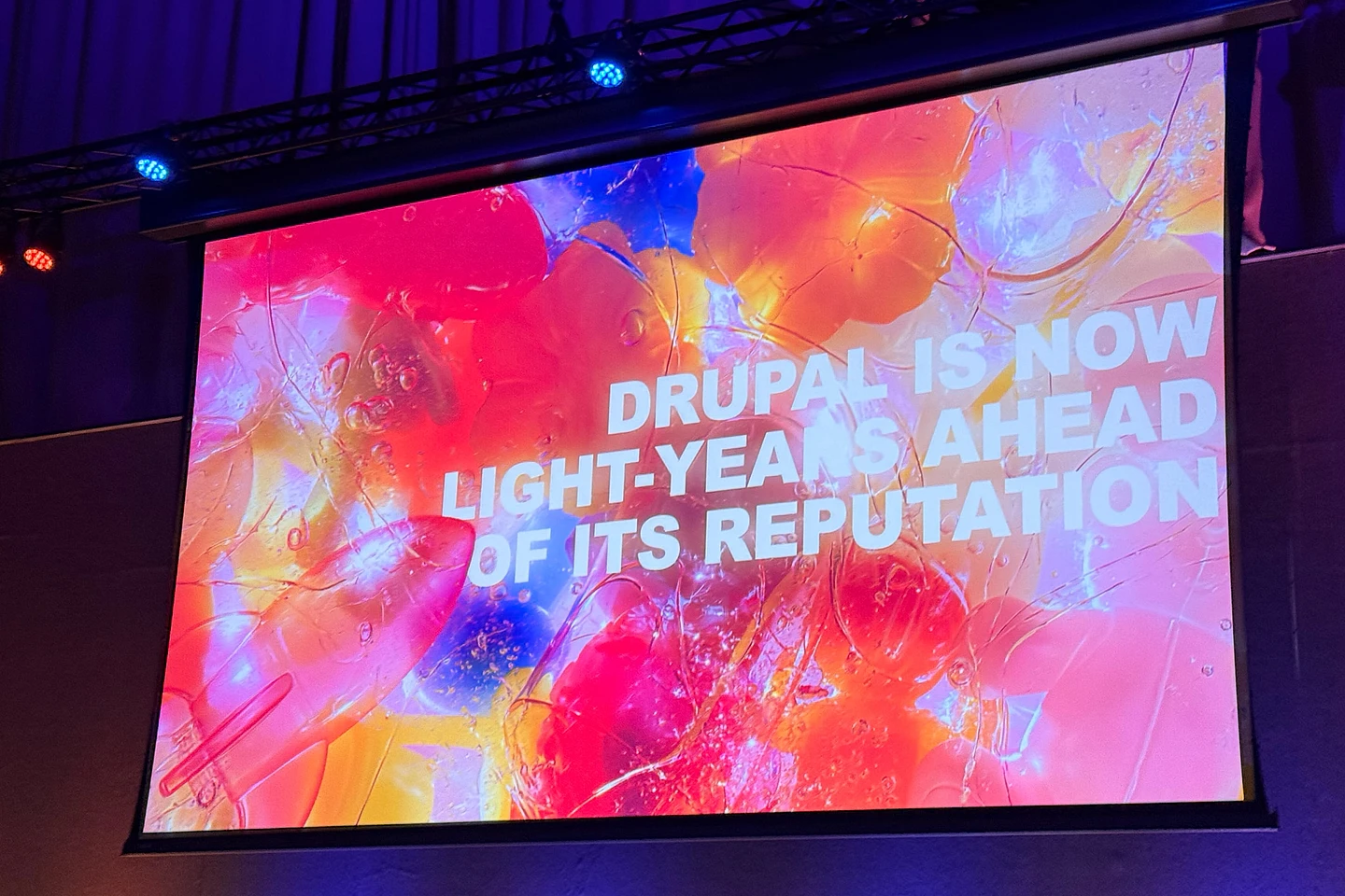 Large projection screen displaying colorful abstract background with text about Drupal being light-years ahead of its reputation.