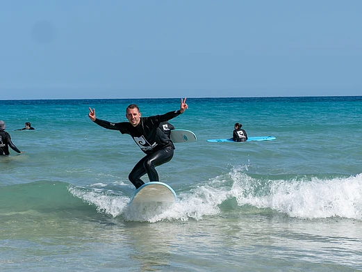 Participant surfing in the ocean during the TYPO3 Surf Camp in Fuerteventura, an event combining coding, mentorship, and community activities for young professionals.