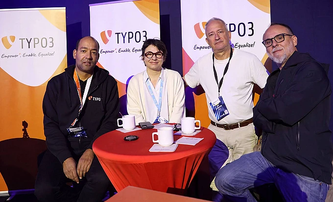 Four professionals seated at a red table at a TYPO3 booth with branded backdrops