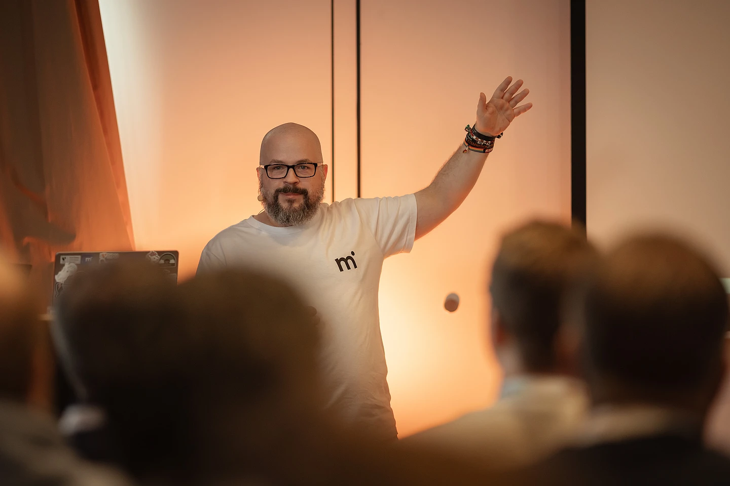 Martin Helmich, wearing a white T-shirt, gestures toward the screen while presenting to an audience.