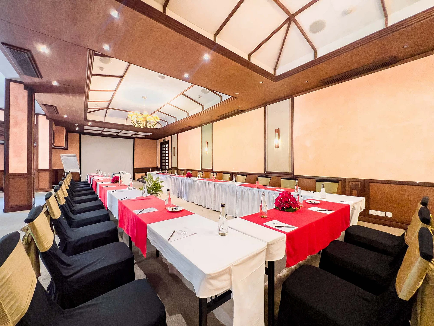 Modern conference room with U-shaped table setup, red and white linens, wooden beams, skylight ceiling, and gold chair covers