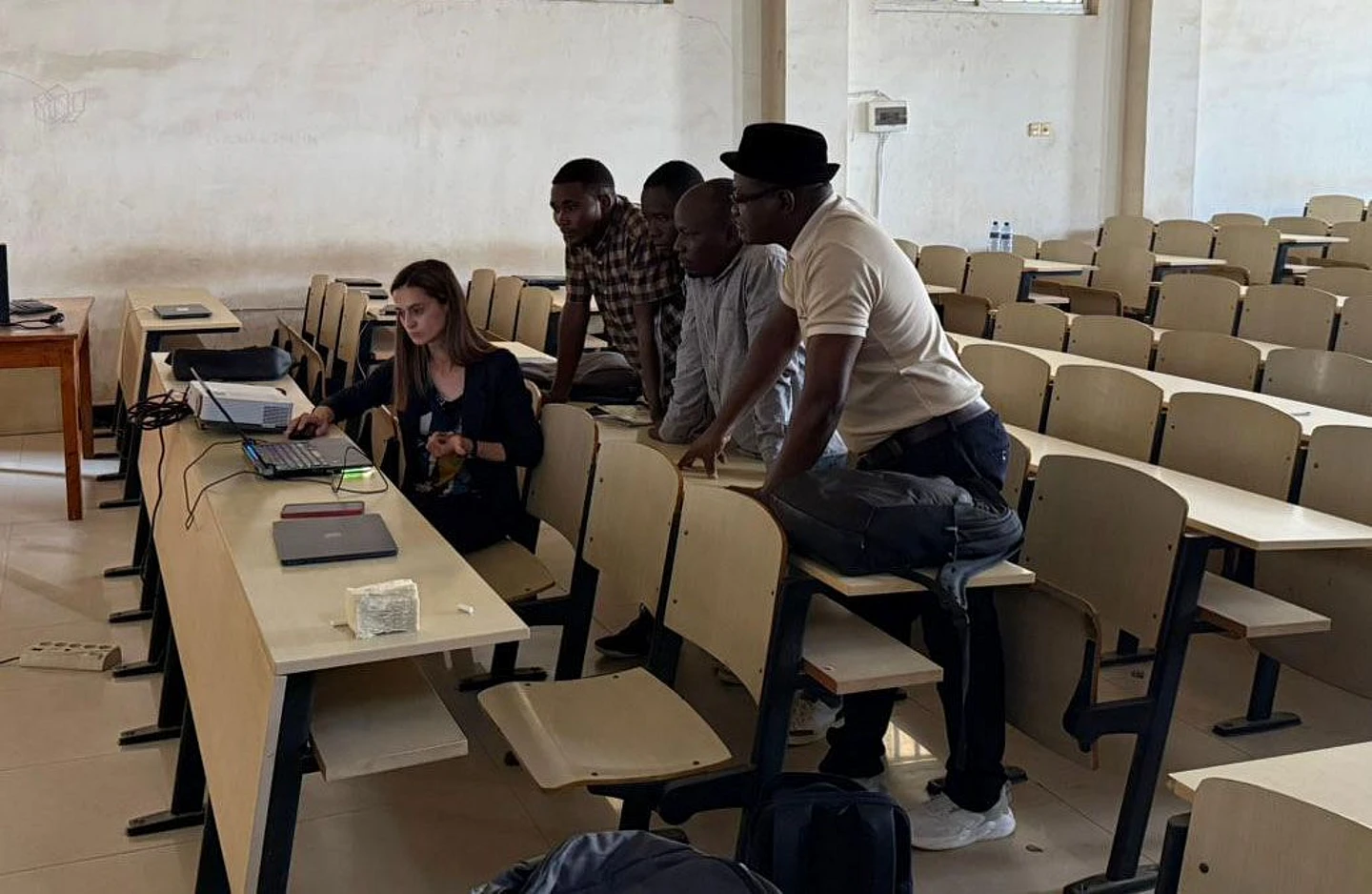 Group of five people in a lecture hall gathered around a laptop for a discussion or presentation