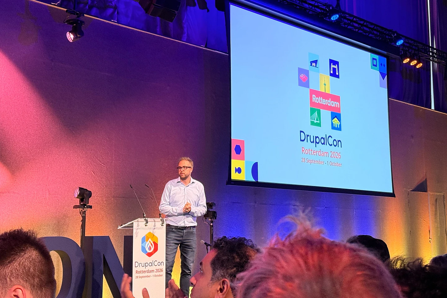 Speaker presenting at DrupalCon Rotterdam 2026 conference on stage with colorful logo displayed on large screen