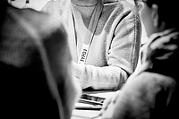 Person wearing TYPO3 lanyard in black and white photo, surrounded by others in casual setting