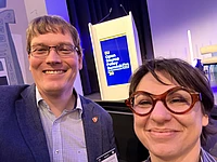 Two people smiling at EU Open Source Policy Summit 2023 event with blue and yellow branding backdrop
